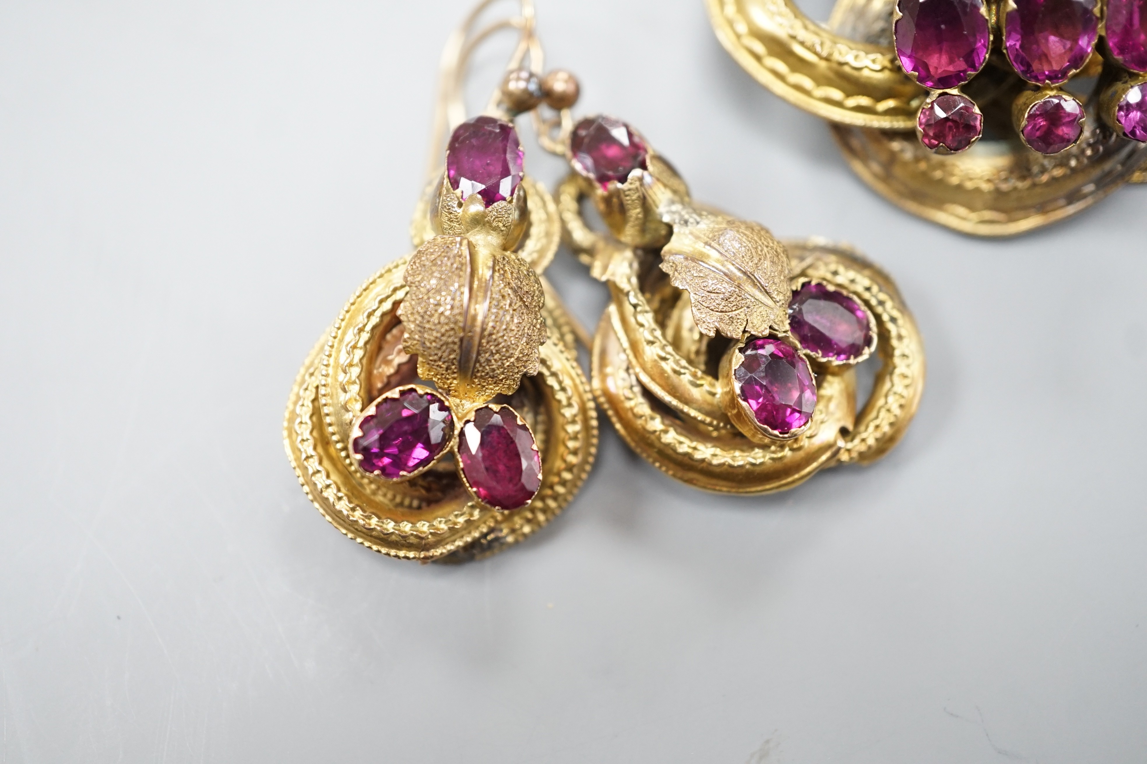 A Victorian yellow metal, oval and round cut garnet set demi parure, comprising a scroll work brooch and pair of matching earrings(a.f.), brooch, 38mm, gross weight 14 grams.